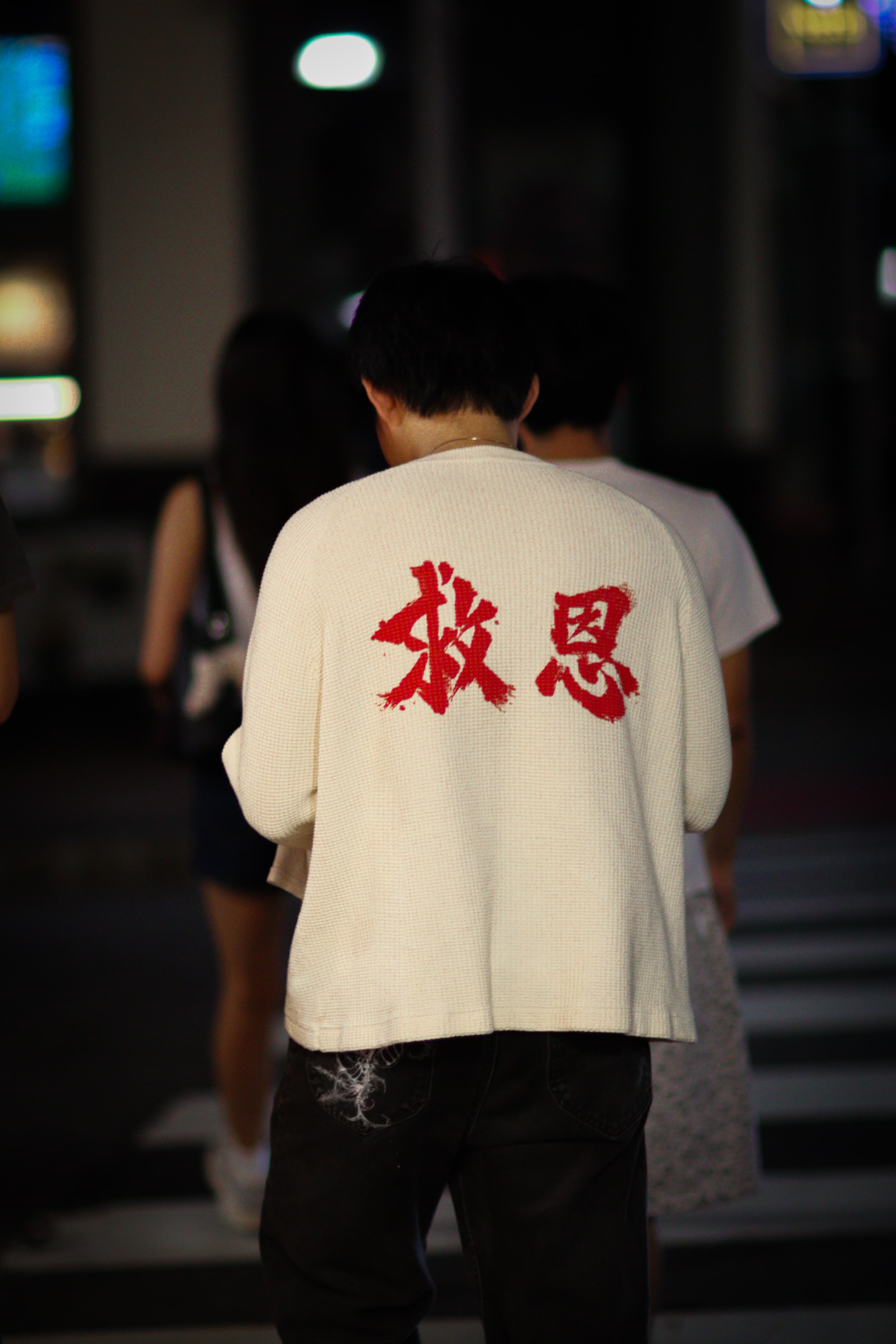 On-model, back, walking through a busy street at night — candid, in motion.