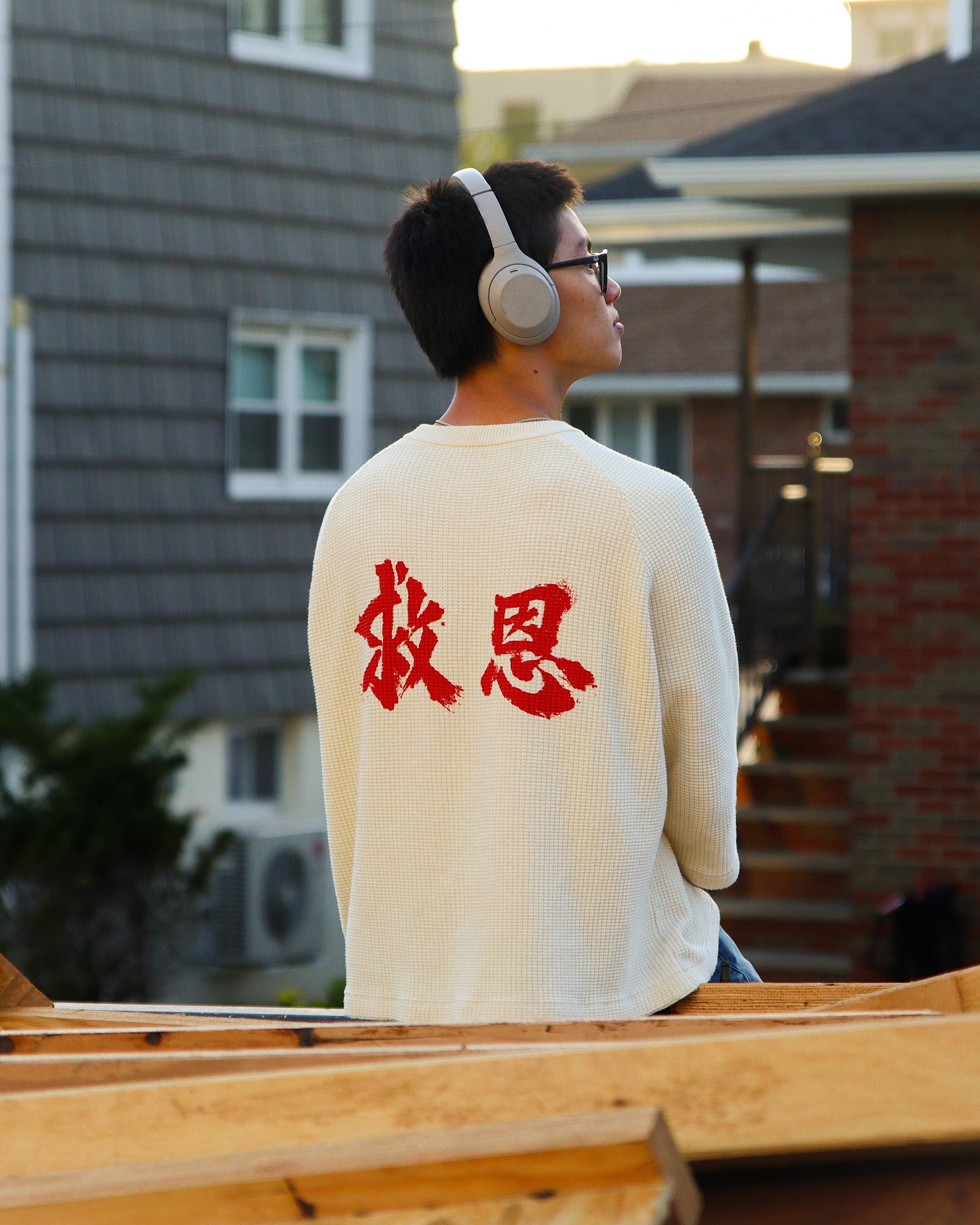 On-model, back, seated on a rooftop at golden hour, headphones on — a candid moment.