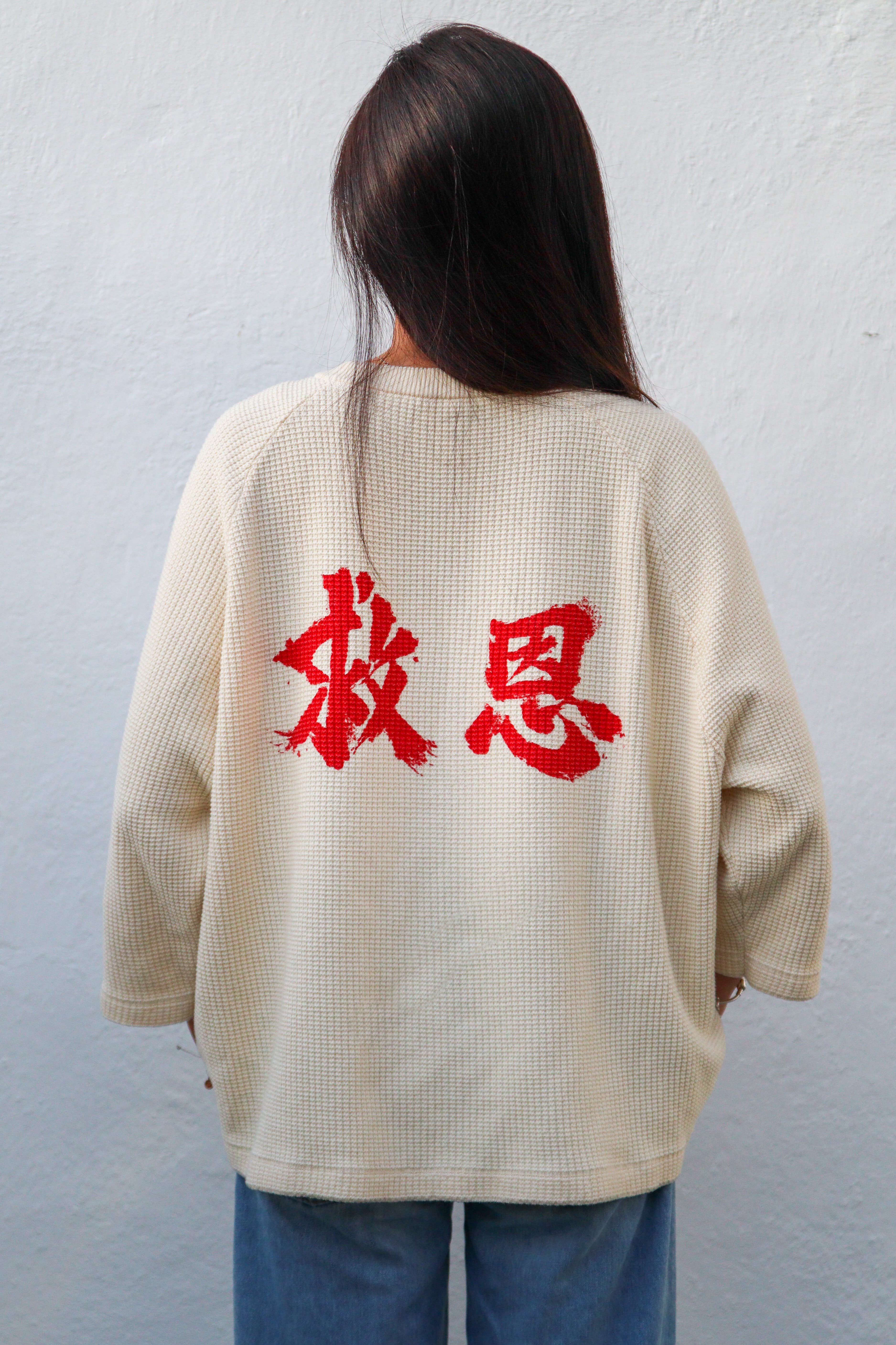 On-model, female, back, straight on, studio lit: the 救恩 mark in red across the cream waffle knit.