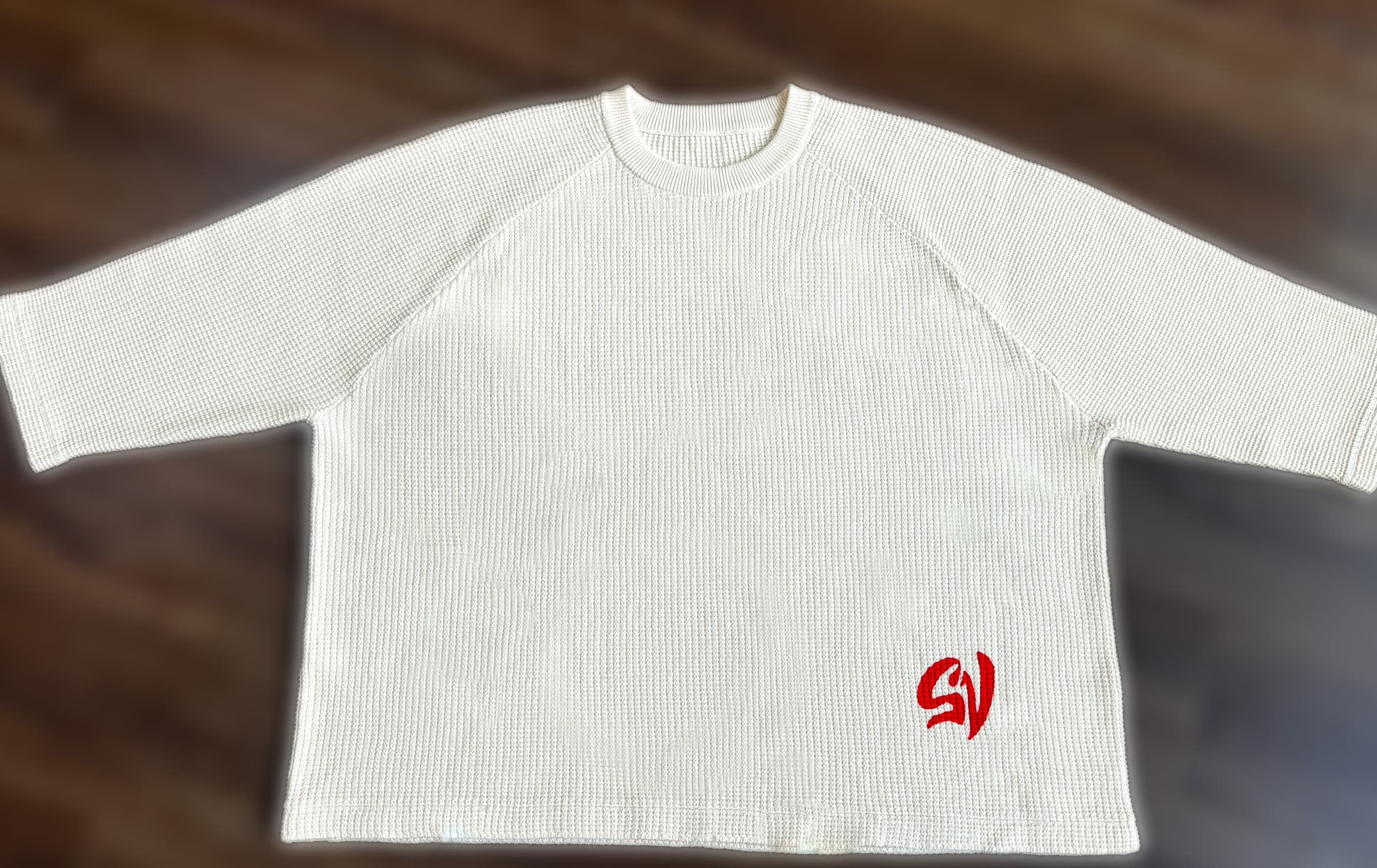 Flat-lay of the garment, front, on a wood floor.