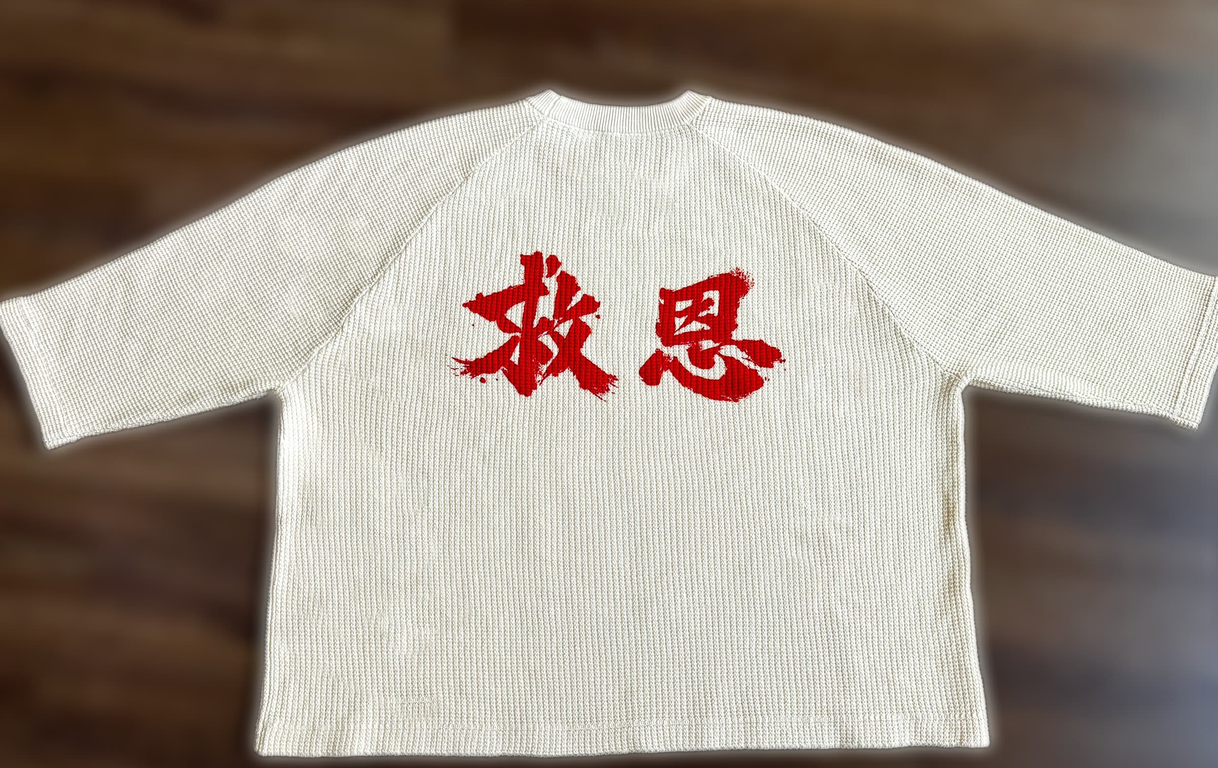 Flat-lay of the garment, back, showing the 救恩 mark, on a wood floor.